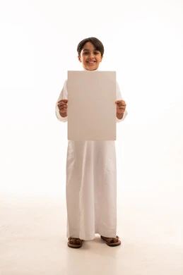Looking at camera with pleased gestures, white square mockup, blank billboard, use of illustrative panels, portrait of smiling Saudi Arabian Gulf boy wearing traditional thobe standing straight and holding a white square panel, full body, white background