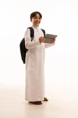 Searching for useful and important information, portrait of a Saudi Arabian Gulf boy wearing traditional dress and a backpack holding a tablet, integrating technology with learning, attending e-learning courses, full body image, white background