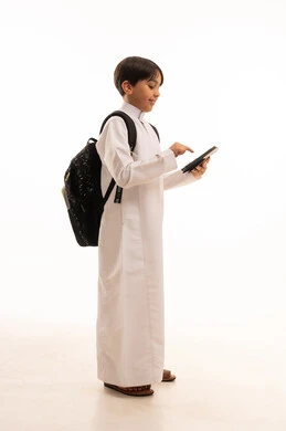 Searching for useful and important information, portrait of a Saudi Arabian Gulf boy wearing traditional dress and a backpack holding a tablet, integrating technology with learning, attending e-learning courses, full body image, white background