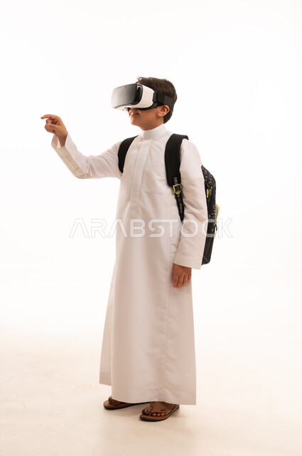 الدراسة عبر المنصات تعليمية، محاكاة العالم الخيالي، بورتريه لطالب عربي خليجي سعودي يرتدي الثوب التقليدي وحقيبة الظهر المدرسية يضع نظارة الفي آر، نشاطات الواقع الافتراضي، صورة الجسم بالكامل، خلفية بيضاء