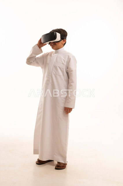 تعابير الاندماج والتركيز، محاكاة العالم الخيالي والنظر الى الافلام الواقعيه، التطور التقني والتكنولوجي، بورتريه لولد عربي خليجي سعودي يرتدي الثوب التقليدي ينظر من خلال نظارات ثلاثية الأبعاد (الفي ار),  الجسم بالطول الكامل، خلفيه بيضاء