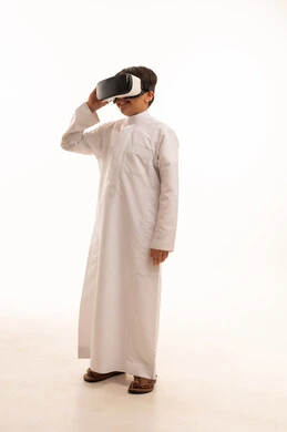 تعابير الاندماج والتركيز، محاكاة العالم الخيالي والنظر الى الافلام الواقعيه، التطور التقني والتكنولوجي، بورتريه لولد عربي خليجي سعودي يرتدي الثوب التقليدي ينظر من خلال نظارات ثلاثية الأبعاد (الفي ار),  الجسم بالطول الكامل، خلفيه بيضاء