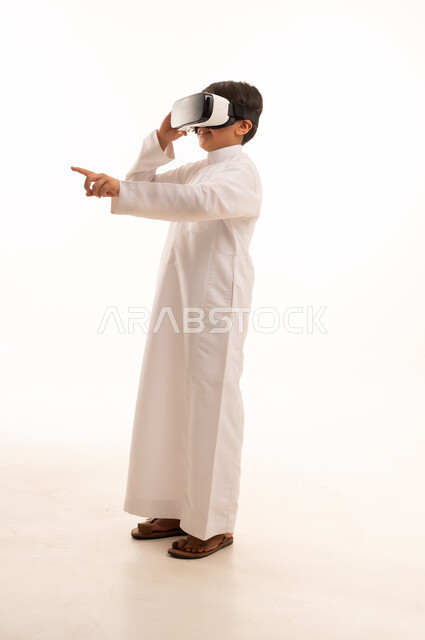 تعابير الاندماج والتركيز، محاكاة العالم الخيالي والنظر الى الافلام الواقعيه، التطور التقني والتكنولوجي، بورتريه لولد عربي خليجي سعودي يرتدي الثوب التقليدي ينظر من خلال نظارات ثلاثية الأبعاد (الفي ار),  الجسم بالطول الكامل، خلفيه بيضاء