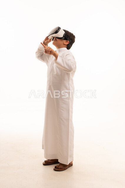 محاكاة العالم الخيالي والنظر الى الافلام الواقعيه، تعابير الاندماج والتركيز، التطور التقني والتكنولوجي، بورتريه لولد عربي خليجي سعودي يرتدي الثوب التقليدي ينظر من خلال نظارات ثلاثية الأبعاد (الفي ار),  الجسم بالطول الكامل، خلفيه بيضاء