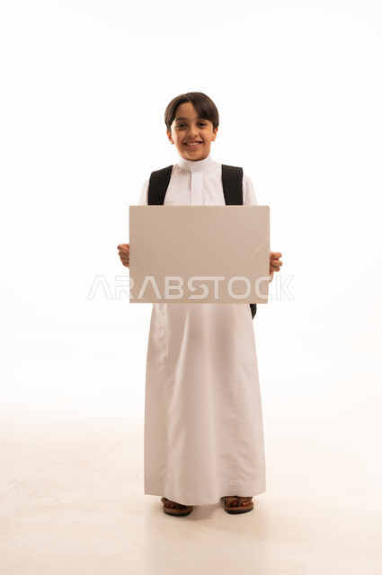 موك اب مستطيل ابيض، الاعلان عن بداية عام دراسي جديد في المدارس السعودية المتقدمة، بورتريه لطالب عربي خليجي سعودي يرتدي الثوب التقليدي وحقيبة الظهر يحمل بيده لوح اعلاني فارغ، صورة لكامل الجسم، خلفية بيضاء