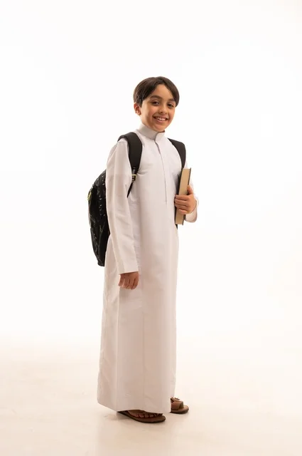 The concept of hard work to achieve success, educational scientific curricula, the concept of returning to school, a portrait of a Saudi Arabian Gulf student wearing traditional clothing, carrying a school backpack and holding a book in his hand, a full body image, a white background