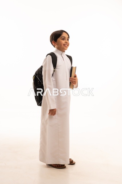 مفهوم الاجتهاد للوصول إلى النجاح، المناهج العلمية التعليمية، مفهوم العودة إلى المدارس، بورتريه لطالب عربي خليجي سعودي يرتدي الثوب التقليدي يحمل حقيبة الظهر المدرسية ويحمل بيده كتاب، صورة لكامل الجسم، خلفية بيضاء