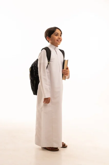 The concept of hard work to achieve success, educational scientific curricula, the concept of returning to school, a portrait of a Saudi Arabian Gulf student wearing traditional clothing, carrying a school backpack and holding a book in his hand, a full body image, a white background