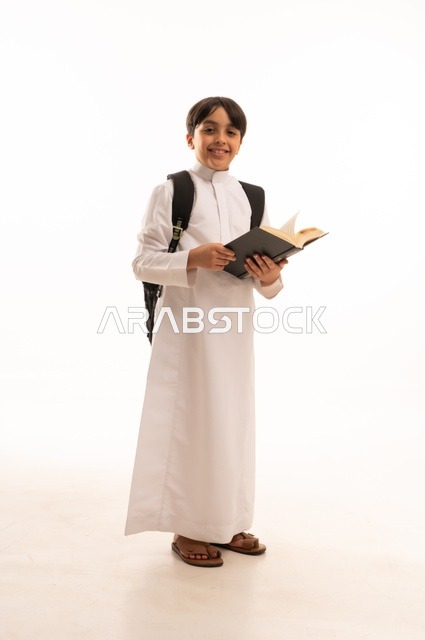 أهمية القراءة في توسيع آفاق المعرفة وزيادة المعلومات، الاجتهاد للوصول إلى النجاح، المناهج العلمية التعليمية، مفهوم العودة إلى المدارس، بورتريه لطالب عربي خليجي سعودي يرتدي الثوب التقليدي يحمل حقيبة الظهر المدرسية ويحمل بيده كتاب، صورة لكامل الجسم، خلفية بيضاء