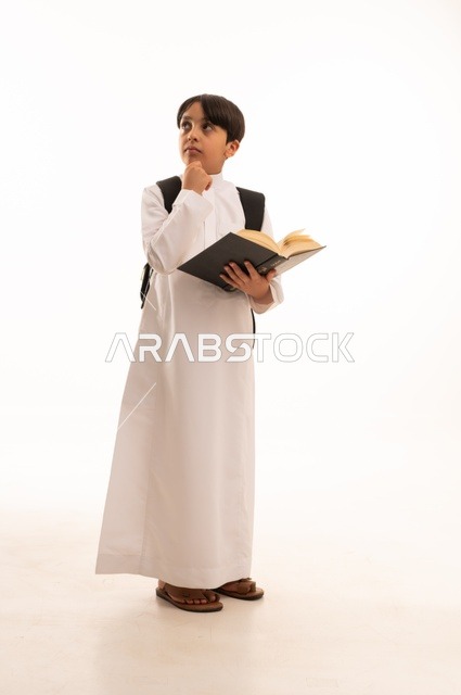 Back to school concept, educational science curricula, portrait of a Saudi Arabian Gulf student wearing traditional dress carrying a school backpack, putting his hand on his chin with questioning and surprised gestures and reading a book, full body image, white background