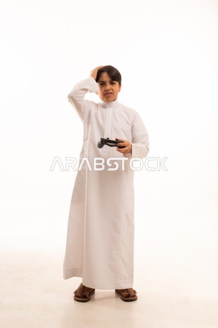 Using a modern and advanced technological device, having a good time playing video games, portrait of a Saudi Arabian boy wearing traditional clothing holding a joystick and placing his hand on his head with gestures of loss and defeat, full body, white background