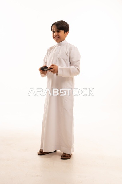 Having fun playing video games, portrait of a Saudi Arabian boy wearing traditional clothing holding a joystick, gestures of enjoyment and integration, using a modern and advanced technological device, white background