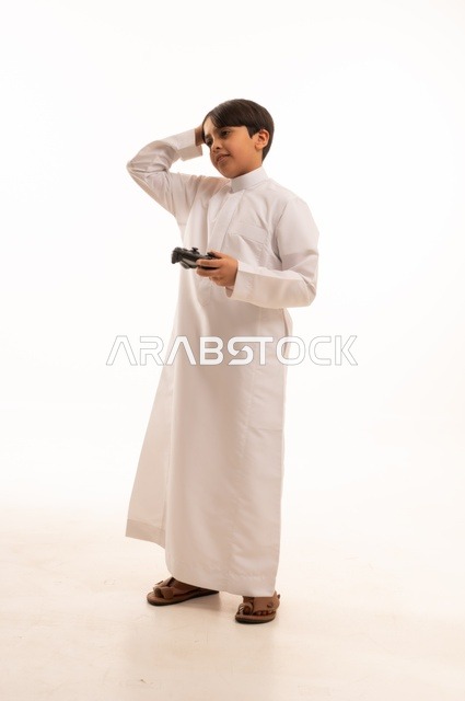 Using a modern and advanced technological device, having a good time playing video games, portrait of a Saudi Arabian boy wearing traditional clothing holding a joystick and placing his hand on his head with gestures of loss and defeat, full body, white background