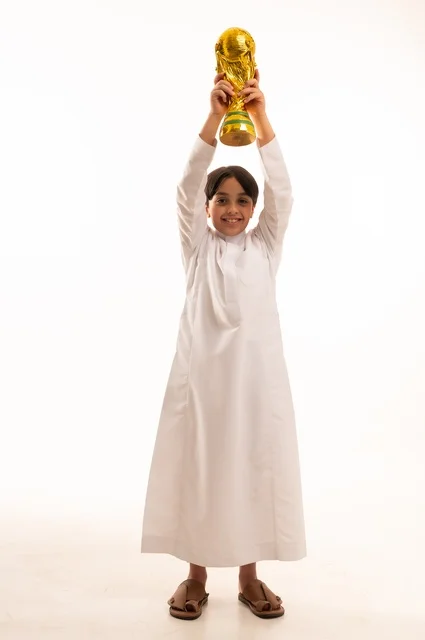 تعابير الفرح والسرور والحماس للمنافسة، مفهوم الربح والفوز، تشجيع الفريق السعودي، التتويج بالبطولة والحصول على المركز الأول، بورتريه لولد عربي خليجي سعودي يرتدي الثوب التقليدي يحمل بيده كأس كرة قدم ذهبي, صورة الجسم بالطول الكامل
, خلفية بيضاء