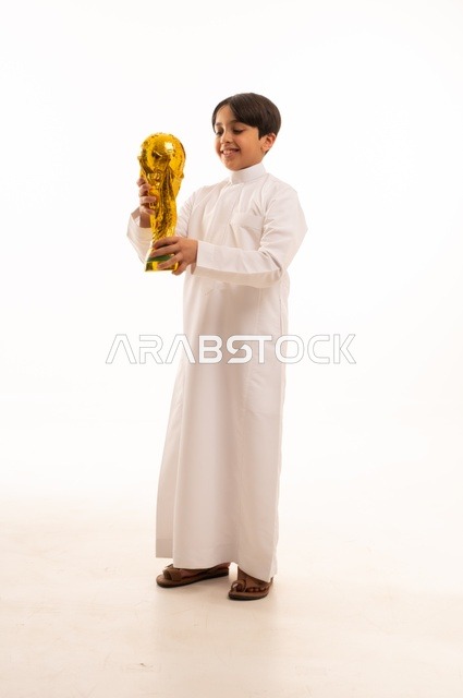 تعابير الفرح والسرور والحماس للمنافسة، مفهوم الربح والفوز، تشجيع الفريق السعودي، التتويج بالبطولة والحصول على المركز الأول، بورتريه لولد عربي خليجي سعودي يرتدي الثوب التقليدي يحمل بيده كأس كرة قدم ذهبي, صورة الجسم بالطول الكامل
, خلفية بيضاء