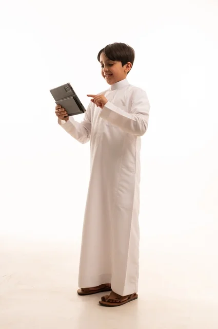 مفهوم التعليم الالكتروني، متابعة الدروس عن بعد عن طريق الانترنت، المناهج العلمية التعليمية،  بورتريه لولد عربي خليجي سعودي يرتدي الثوب التقليدي وحقيبة الظهر يحمل بيده الجهاز اللوحي، استخدام جهاز تقني حديث ومتطور، الجسم بالطول الكامل, خلفية بيضاء