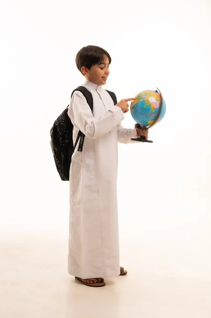 الاهتمام بدراسة العلوم الجغرافية، توسيع الآفاق وفهم التنوع الثقافي والطبيعي، أهمية التعليم في تطوير المجتمع السعودي، بورتريه لطالب عربي خليجي سعودي يرتدي الثوب التقليدي وحقيبة الظهر يحمل بيده مجسم الكرة الأرضية، الجسم بالطول الكامل، خلفية بيضاء