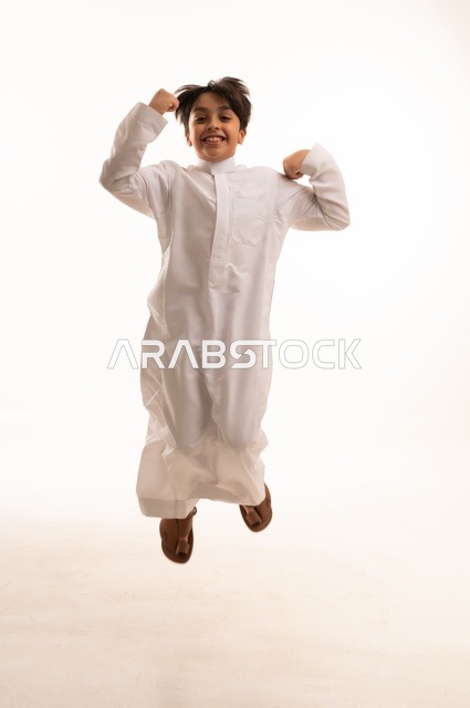 The concept of fun and play, jumping high with gestures of happiness and pleasure, portrait of a Saudi Arabian Gulf boy wearing traditional dress jumping in the air, having a fun and entertaining time, full body, white background