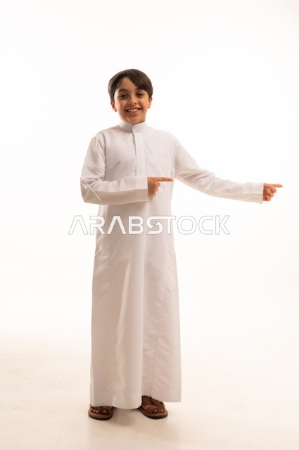 ايماءات تحديد موقع معين، حركات تدل على هذا المكان (هنا)، بورتريه لولد عربي خليجي سعودي يرتدي الثوب التقليدي ويشير باصبع السبابة الى شيء ما، صورة الجسم بالطول الكامل، خلفية بيضاء