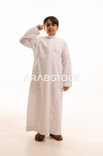 ايماءات تحديد موقع معين، حركات تدل على هذا المكان (هنا)، بورتريه لولد عربي خليجي سعودي يرتدي الثوب التقليدي ويشير باصبع السبابة الى شيء ما، صورة الجسم بالطول الكامل، خلفية بيضاء