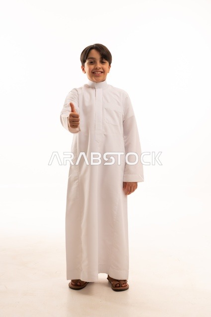 ايماءات الرضى والقبول، مفهوم الاعجاب والتقييم الايجابي، الاهتمام بالأناقة والمظهر الخارجي، بورتريه لولد عربي خليجي سعودي يرتدي الثوب التقليدي يرفع اصبع الابهام بتعابير السرور والسعادة، الجسم بالطول الكامل، خلفية بيضاء