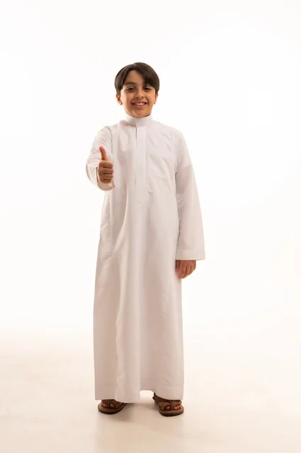 Gestures of satisfaction and acceptance, the concept of admiration and positive evaluation, interest in elegance and outward appearance, portrait of a Saudi Arabian Gulf boy wearing traditional dress raising his thumb with expressions of pleasure and happiness, full body, white background