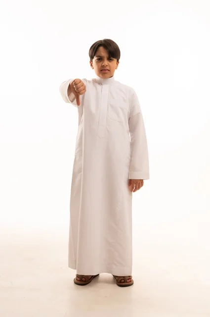 مفهوم التقييم السلبي والانزعاج، القلق والفشل في تحقيق أمر ما، بورتريه لولد عربي خليجي سعودي يرتدي الثوب التقليدي يرفع اصبع الابهام بتعابير الرفض وعدم القبول والرضا، الجسم بالطول الكامل، خلفية بيضاء