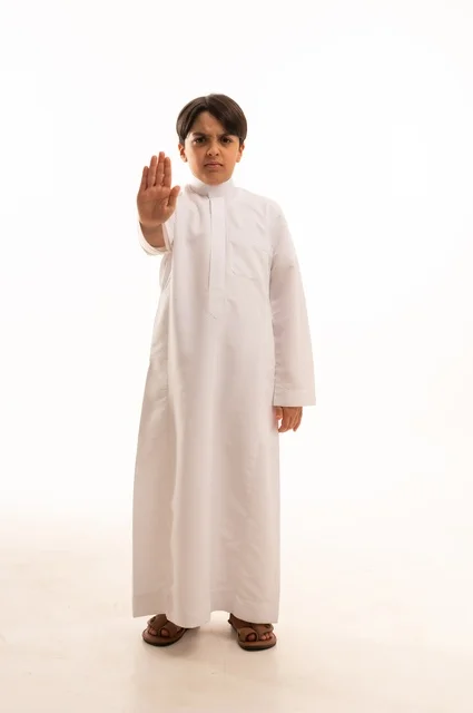 الأمر بالتوقف عن فعل شيء ما، مفهوم الرفض والإمتناع، بورتريه لولد عربي خليجي سعودي يرتدي الثوب التقليدي يمد يده نحو الأمام مع رفع الكف بإيماءات النهي عن فعل امر ما, تعابير الحزم والجدية, الجسم بالطول الكامل، خلفية بيضاء