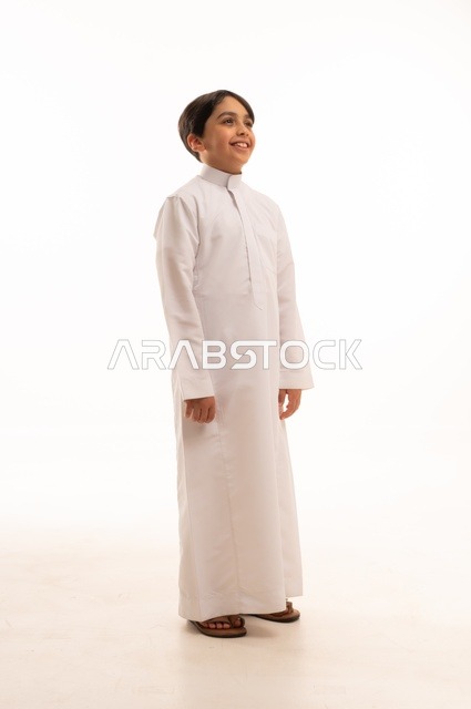 الاهتمام بالأناقة والمظهر الخارجي، مفهوم الثقة بالنفس، التقاط الصور الشخصية للوثائق الرسمية، بورتريه لولد عربي خليجي سعودي يرتدي الثوب التقليدي يقف بإيماءات السرور والسعادة، الجسم بالطول الكامل، خلفية بيضاء