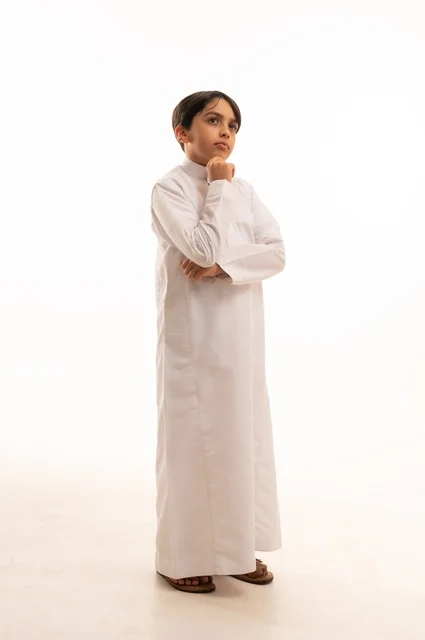 النظر الى شيء ما بايماءات التفكير، الاهتمام بالأناقة والمظهر الخارجي، مفهوم الثقة بالنفس، بورتريه لولد عربي خليجي سعودي يرتدي الثوب التقليدي يضع يده على ذقنه، الجسم بالطول الكامل، خلفية بيضاء