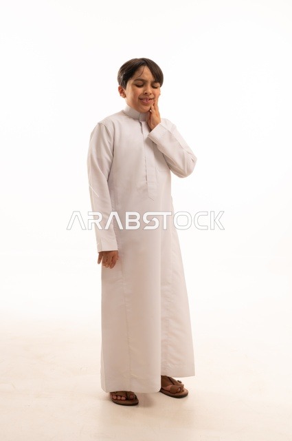 تسوس الأضراس وإلتهاب اللثه ,وجع الأسنان والحاجه لزيارة الطبيب، طلب العلاج والمساعده، بورتريه لولد عربي خليجي سعودي يرتدي الثوب التقليدي يضع يده على فمه، صورة الجسم بالطول الكامل، خلفية بيضاء