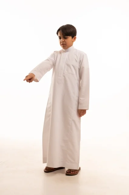Gestures indicating this place (here), gestures to determine a specific location, portrait of a Saudi Arabian Gulf boy wearing traditional thobe and pointing with his index finger at something with an angry expression, full-length body image, white background