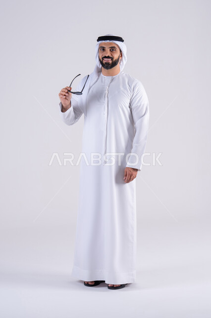 الاهتمام بالاناقة والاهتمام بالمظهر الخارجي،  احدث صيحات الموضه ،تعابير السرور والسعاده ، ارتداء النظارات الشمسيه ،بورتريه لرجل عربي خليجي اماراتي يرتدي الكندوره  والغتره، يقوم بارتداء نظاره سوداء بإيماءات الثقة بالنفس