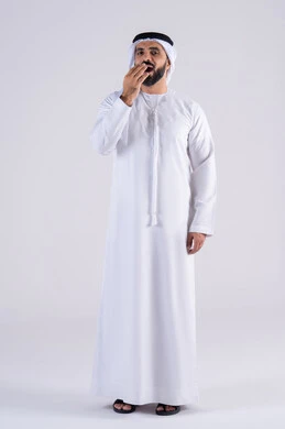 Feeling tired and in need of rest, feeling lazy and lethargic, portrait of an Arab, Gulf, Emirati man wearing a kandura and ghutra, placing his hands on his face with sleepy gestures, expressions of sleepiness and exhaustion