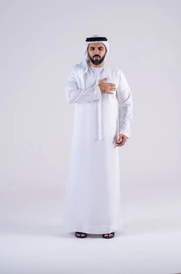 Angina pectoris pain, sudden heart attacks, chest and heart palpitations, portrait of an Arab Gulf Emirati man wearing a kandura and ghutra, placing his hand on his heart with gestures of pain and suffering.