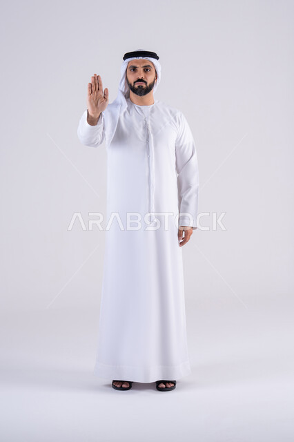 Expressions of refusal and abstention, command to stop doing something, portrait of an Arab Gulf Emirati man wearing a kandura and ghutra, raising his hand with gestures indicating prohibition, feelings of annoyance and anger.