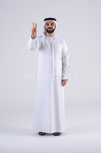 النجاح وتحقيق الأهداف، تعابير السرور والسعادة،بورتريه لرجل عربي خليجي اماراتي يرتدي الكندوره والغتره ينظر إلى الكاميرا بايماءات وجه ويدين تدل على الفوز والإنتصار