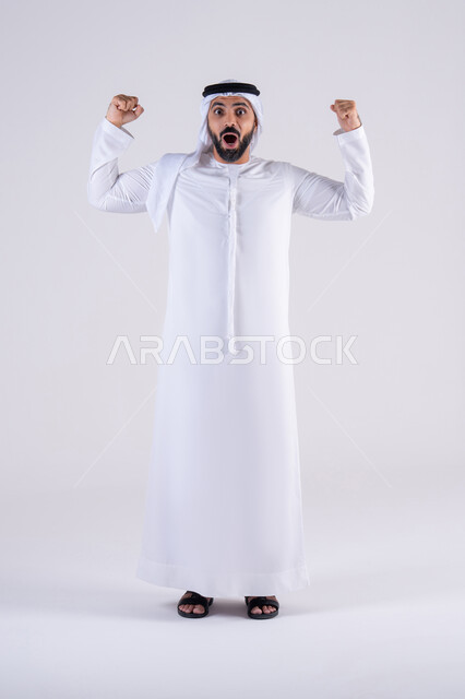 مفهوم الفرح بالنصر والفوز، تعابير السرور والسعادة،النجاح وتحقيق الأهداف،  بورتريه لرجل عربي خليجي اماراتي يرتدي الكندوره والغتره يرفع يديه بإيماءات الحماس