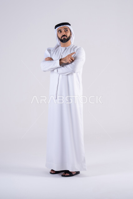 Looking aside with focus gestures, portrait of an Arab Gulf Emirati man wearing a kandura and ghutra, pointing his index finger to the side at something, expressions specifying this place here, specifying a specific location