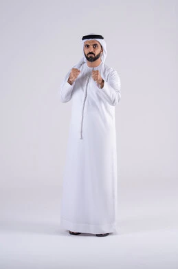 تعزيز صحة العظام والمفاصل، ممارسة رياضة الدفاع عن النفس، زيادة قدرة العضلات على التحمل، إتقان فنون الملاكمة، بورتريه لرجل عربي خليجي اماراتي يرتدي الكندوره والغتره يرفع قبضات يده بإيماءات القوة