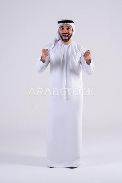 النجاح وتحقيق الأهداف، مفهوم الفرح بالنصر والفوز، تعابير السرور والسعادة، بورتريه لرجل عربي خليجي اماراتي يرتدي الكندوره والغتره يرفع يديه بإيماءات الحماس