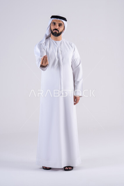 الهدوء وطلب التوقف، بورتريه لرجل عربي خليجي اماراتي يرتدي الكندوره  والغتره ينظر الى الكاميرا بإيماءات الصبر والتأن والتريث، إمهال الوقت والإنتظار للقيام بشيء ما