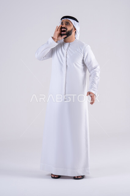 النداء والكلام والتحدث بصوت مرتفع،بورتريه لرجل عربي خليجي اماراتي يرتدي الكندوره والغتره يضع يده على فمه بإيماءات المناداة لشخص ما، دردشة ومحادثات وتواصل اجتماعي