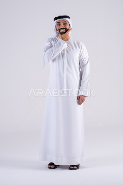 إنتظار مكالمه وإستخدام المايكروفون، التواصل مع الأصدقاء ،بورتريه لرجل عربي إماراتي خليجي يرتدي الكندوره والغتره , يقوم بإيماءات وجه ويدين تدل على إجراء مكالمه هاتفيه, تلقي إتصال , إشارة تعني إتصل بي