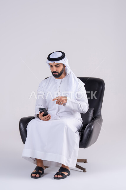 استخدام التقنيات والتكنولوجيا الحديثة بالحياة اليومية ،اجراء مكالمه فيديو ، الدردشة والتحدث مع الأصدقاء،تصفح مواقع وتطبيقات الانترنت، بورتريه لرجل عربي خليجي اماراتي يرتدي الكندوره والغتره، يمسك الجوال بيده