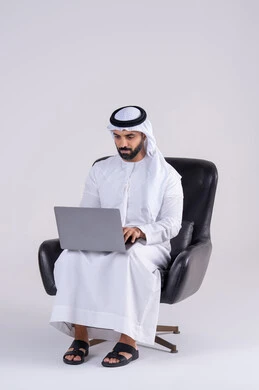 Integrating advanced technology into daily life, using modern technologies in administrative work, completing work tasks remotely, making video calls, portrait of an Arab Gulf Emirati man wearing a kandora and ghutra, sitting on a chair and working on a laptop.