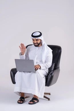 Making video calls, completing work tasks remotely, using modern technologies in administrative work. Portrait of an Arab Gulf Emirati man wearing a kandora and ghutra, sitting on a chair and working on a laptop. Integrating advanced technology into daily life.