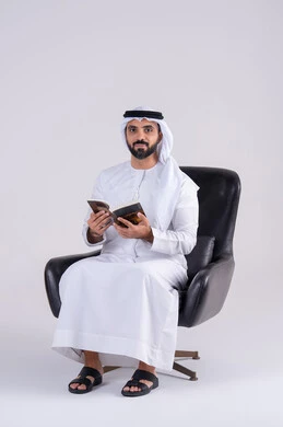 Spending free time educating and learning, acquiring knowledge and science, the concept of literacy, a portrait of an Arab Gulf Emirati man wearing a kandura and ghutra, practicing the hobby of reading useful books in his free time, gestures of contemplation and concentration.