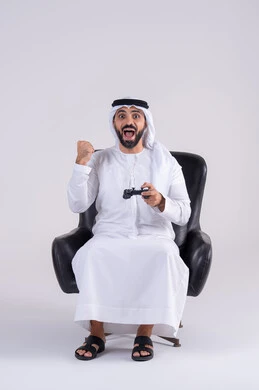 Enjoying modern technology and techniques, raising a fist with a gesture of victory and triumph, the concept of fun and entertainment, having a good time playing video games, a portrait of an Arab Gulf Emirati man wearing a kandora and ghutra holding a joystick.