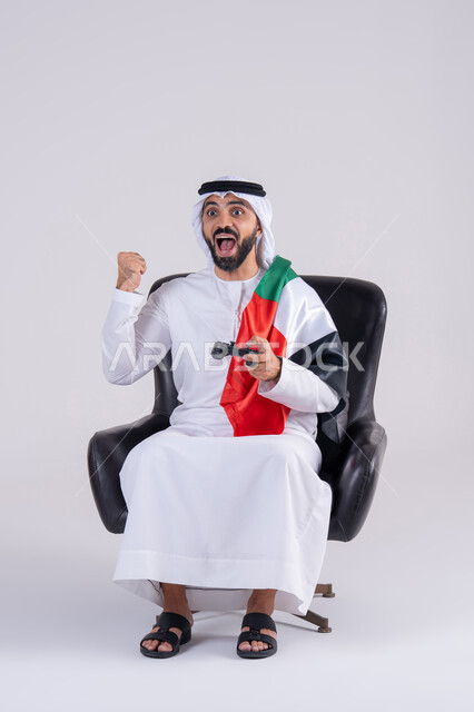 Raising a fist with a victory gesture, having a good time playing video games, enjoying modern technology, the concept of fun and entertainment, a portrait of an Arab Gulf Emirati man wearing a kandura and ghutra holding a joystick and wearing a UAE flag scarf, raising his hand with a gesture of goodness.